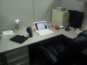 Photo of an empty desk with a laptop, computer speakers, and a coffee mug.
